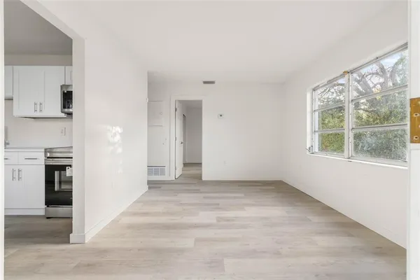 a view of an empty room with kitchen and window