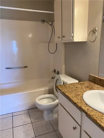 a bathroom with a granite countertop bathtub shower sink vanity and toilet