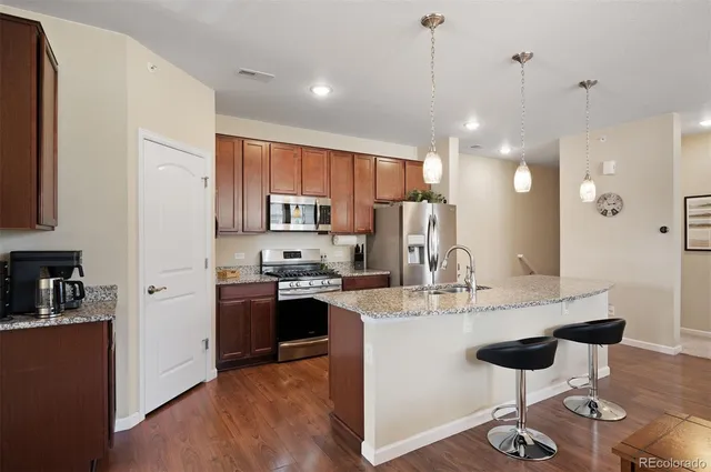a kitchen with stainless steel appliances kitchen island granite countertop a refrigerator a stove a sink dishwasher and a dining table with wooden floor