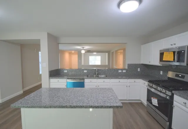 a kitchen with granite countertop a sink a stove top oven and cabinetry