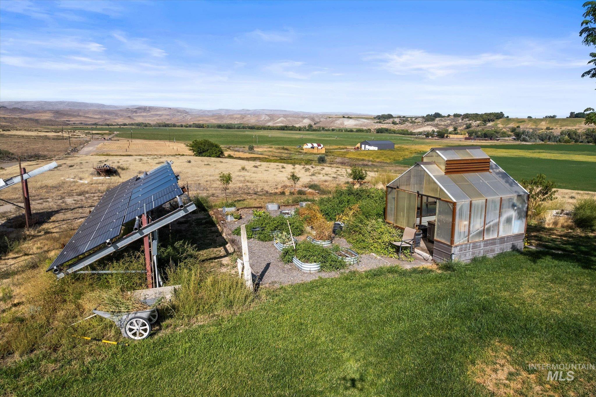 1030 Desert Glen Road Adrian, OR 97901 - Photo 43 of 50 Multiple ground-mounted solar panels, an adjacent greenhouse with a translucent roof, a cultivated garden area with raised beds, and a surrounding expansive grassy lawn