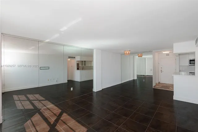 a view of an empty room with wooden floor and a kitchen