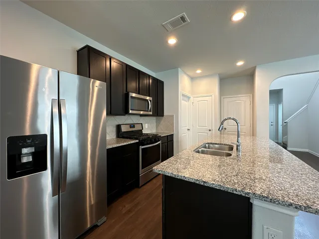 a kitchen with stainless steel appliances granite countertop a refrigerator a sink a stove a microwave and a refrigerator