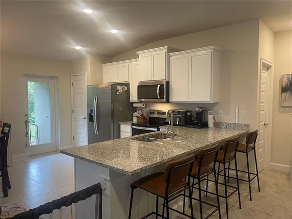 a kitchen with stainless steel appliances granite countertop a stove a refrigerator a sink a dining table and chairs