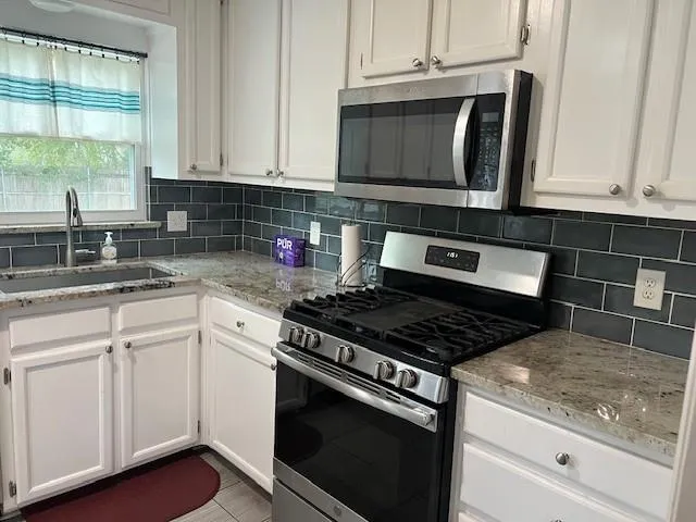 a kitchen with granite countertop white cabinets appliances and a window