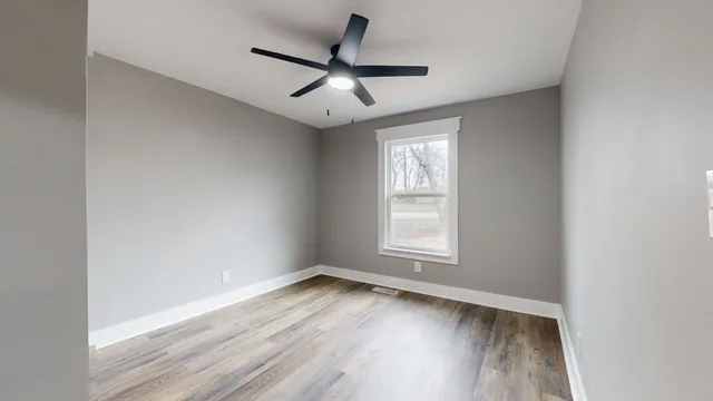 an empty room with wooden floor ceiling fan and window
