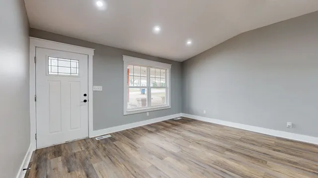 a view of an empty room with wooden floor and a window