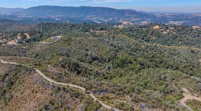 a view of a lush green forest with mountains and a houses