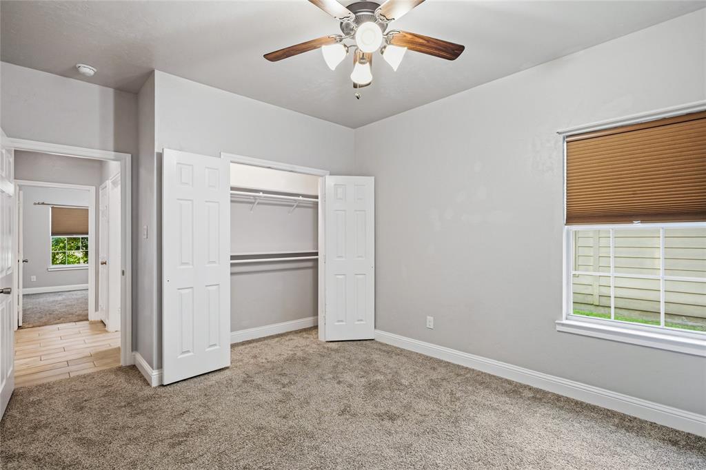 1502 Reed Street Greenville, TX 75401 - Photo 24 of 26 Bedroom featuring plush carpet flooring, a ceiling fan with wood-finish blades, a window with a cellular blind, and a bi-fold door closet with shelving