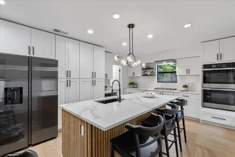 a kitchen with stainless steel appliances kitchen island granite countertop a refrigerator a stove a sink a dining table and chairs