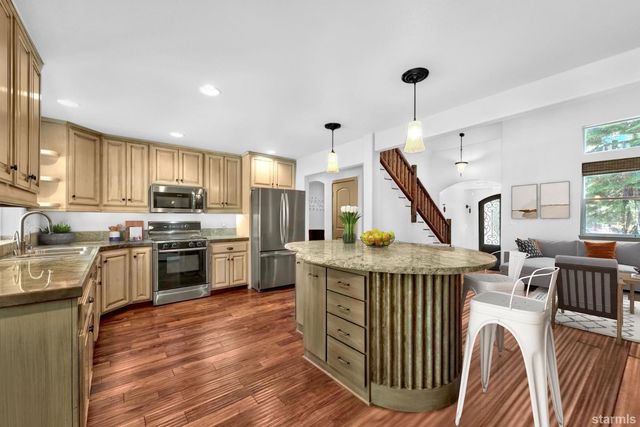a open kitchen with stainless steel appliances granite countertop a stove top oven a sink dishwasher a dining table and chairs with wooden floor