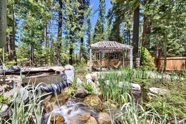 a view of a patio with table and chairs under an umbrella with large trees