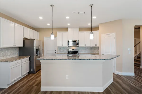 a kitchen with stainless steel appliances granite countertop a sink a stove a refrigerator and island with wooden floor