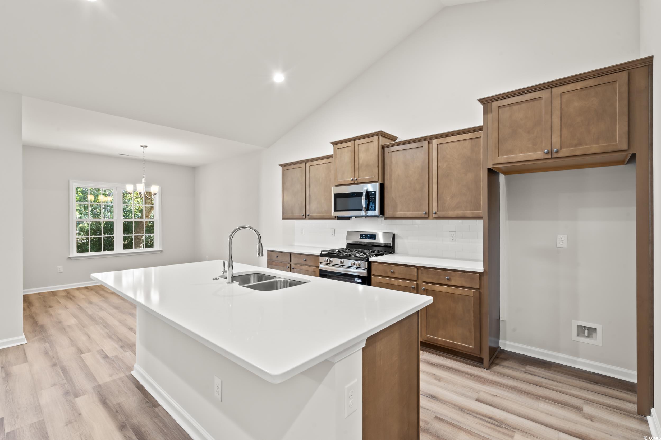 2315 Withers Street Georgetown, SC 29440 - Photo 5 of 29 Kitchen with brown cabinetry, stainless steel appliances, an island with sink, decorative light fixtures, and a chandelier