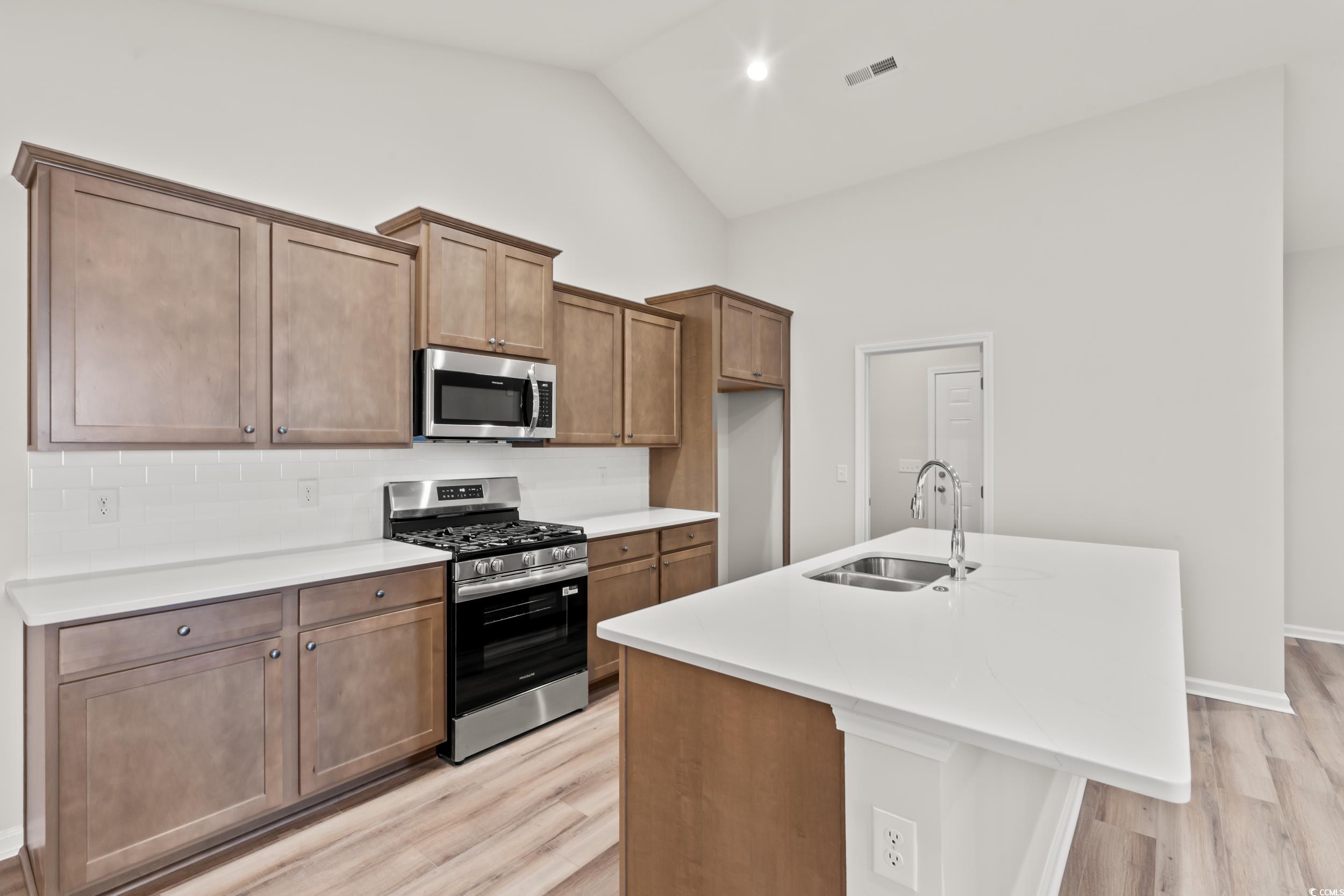 2315 Withers Street Georgetown, SC 29440 - Photo 7 of 29 Kitchen with appliances with stainless steel finishes, a center island with sink, light wood-style floors, brown cabinets, and light stone countertops