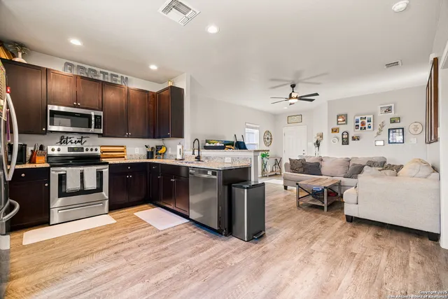 a kitchen with stainless steel appliances kitchen island granite countertop a stove top oven a sink dishwasher a dining table and chairs with wooden floor