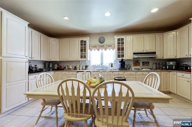 a kitchen with stainless steel appliances kitchen island granite countertop a refrigerator a stove a sink a dining table and chairs with wooden floor