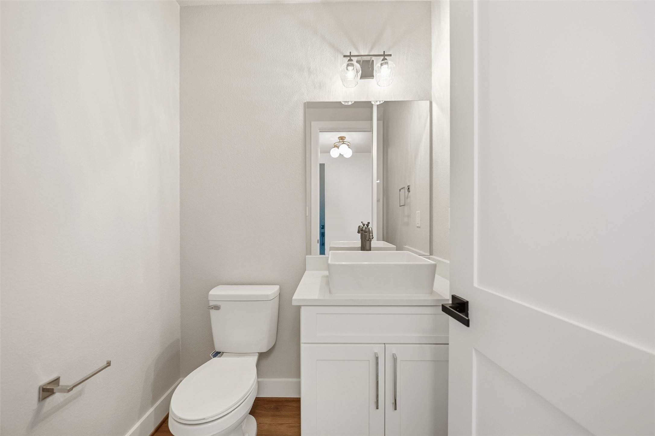 3422 Elser Street Houston, TX 77009 - Photo 11 of 26 This is a modern, compact bathroom featuring a white vanity with a vessel sink, a large mirror, a toilet, and elegant light fixtures, creating a clean and bright atmosphere.