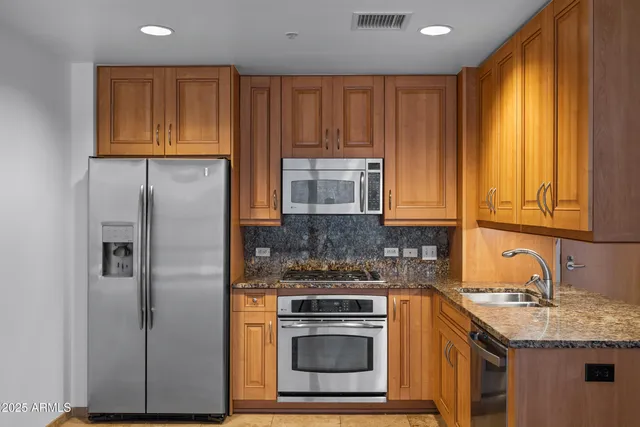 a kitchen with stainless steel appliances granite countertop a stove a sink and a refrigerator with wooden cabinets