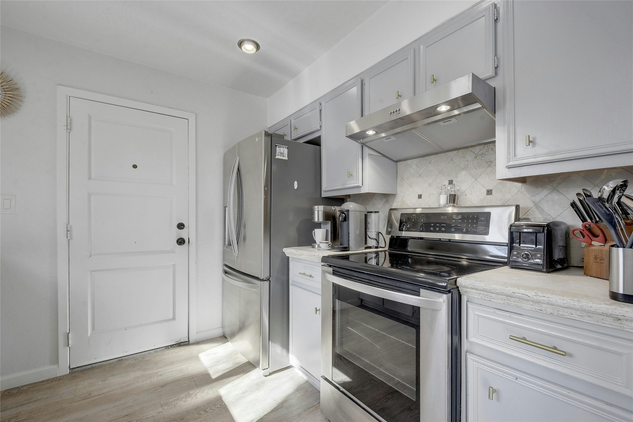 1503 Terrapin Court, Unit B Austin, TX 78746 - Photo 8 of 35 Kitchen with stainless steel appliances, under cabinet range hood, tasteful backsplash, light wood-style floors, and gray cabinetry