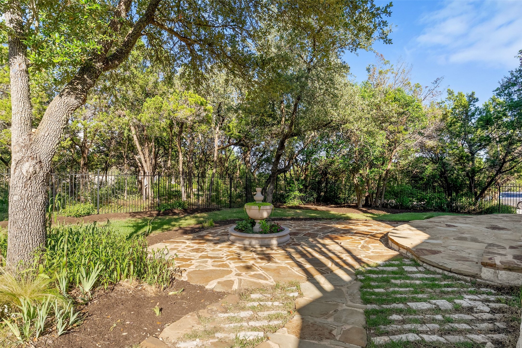 8215 Dark Ridge Cove Austin, TX 78737 - Photo 37 of 40 A tranquil backyard living space features a tiered fountain and natural flagstone patio, embraced by mature trees.