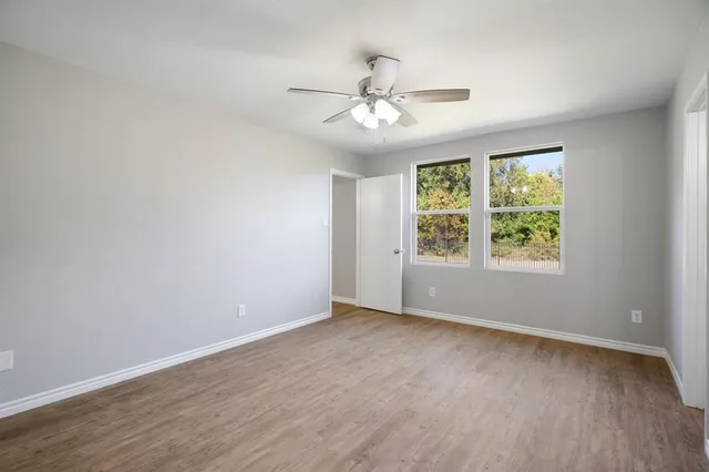 an empty room with wooden floor chandelier fan and windows
