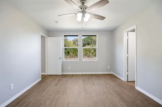 an empty room with wooden floor chandelier fan and windows