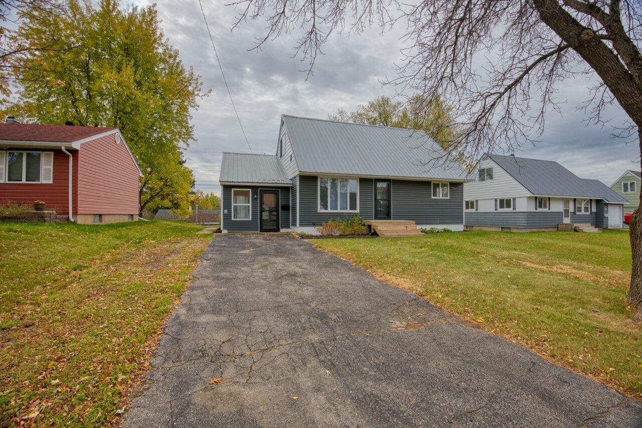 View of front of property featuring a front yard, a metal roof, and asphalt driveway