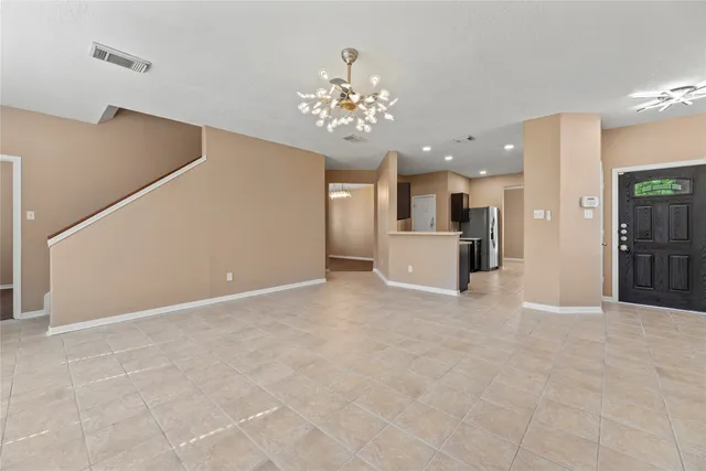 a view of an empty room with kitchen and chandelier