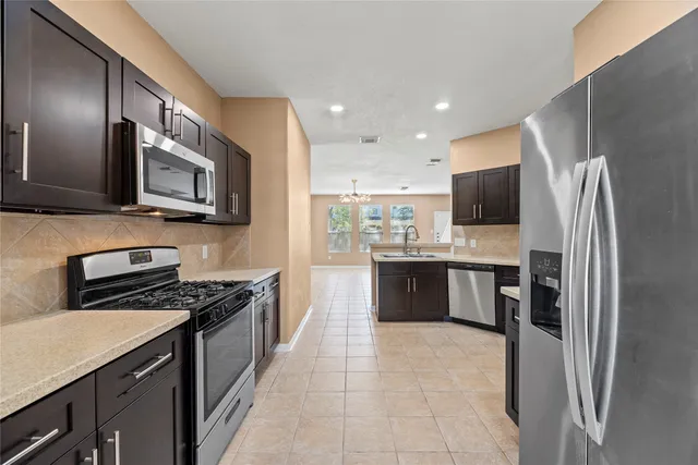 a kitchen with stainless steel appliances granite countertop a stove top oven a sink dishwasher a refrigerator and a microwave oven with large wooden cabinets