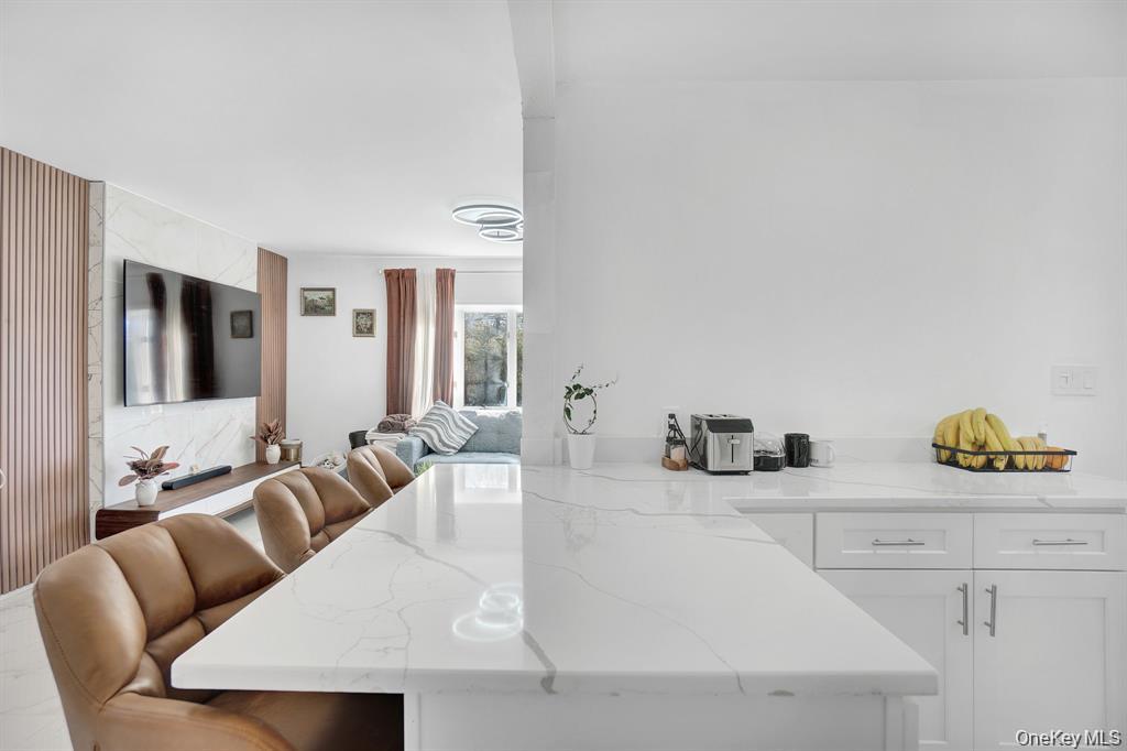 61 South Merrick Road Massapequa, NY 11758 - Photo 11 of 29 Kitchen with a peninsula, light stone countertops, white cabinetry, and a kitchen bar