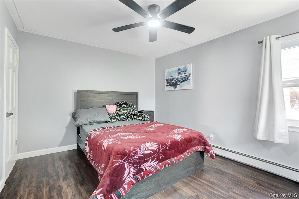 61 South Merrick Road Massapequa, NY 11758 - Photo 16 of 29 Bedroom with baseboard heating, dark wood-style floors, ornamental molding, and a ceiling fan
