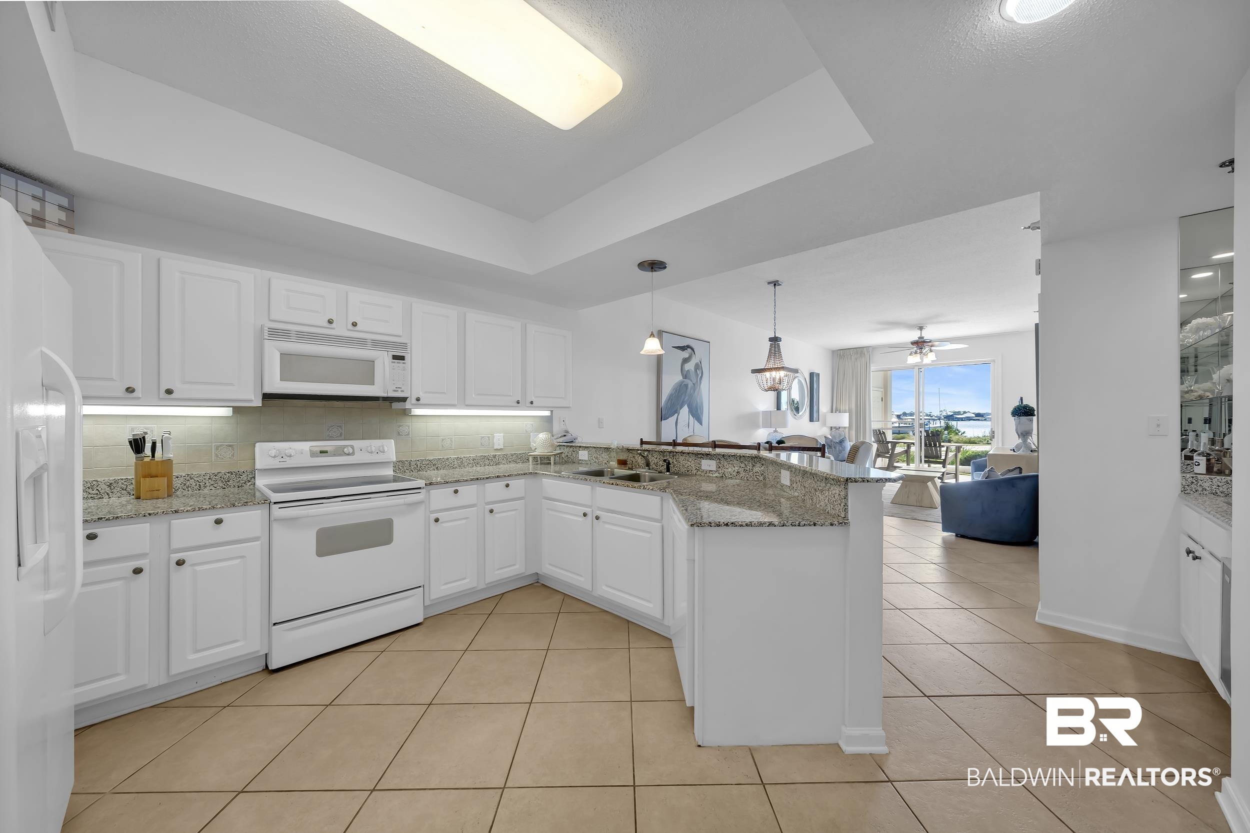 27282 Canal Road, Unit 104 Orange Beach, AL 36561 - Photo 13 of 79 Kitchen with decorative backsplash, white appliances, a raised ceiling, a peninsula, and light stone counters
