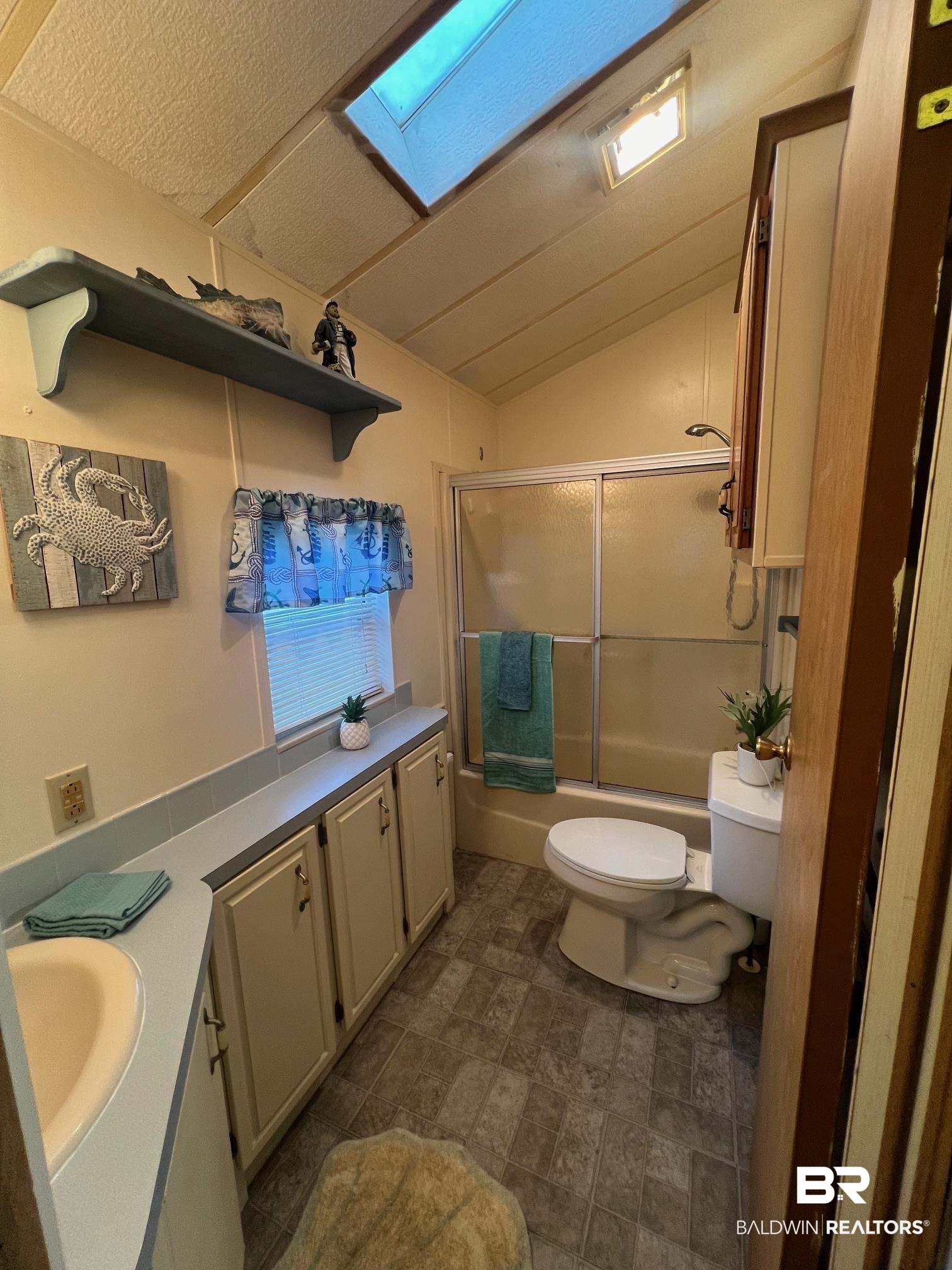 698 Escambia Loop Lillian, AL 36549 - Photo 10 of 16 Full bathroom with vaulted ceiling with skylight, a textured ceiling, shower / bath combination with glass door, vanity, and toilet