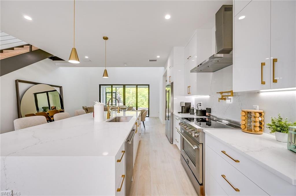 3400 Canal Street Naples, FL 34112 - Photo 8 of 28 Kitchen featuring white cabinetry, wall chimney exhaust hood, premium appliances, light stone countertops, and decorative light fixtures