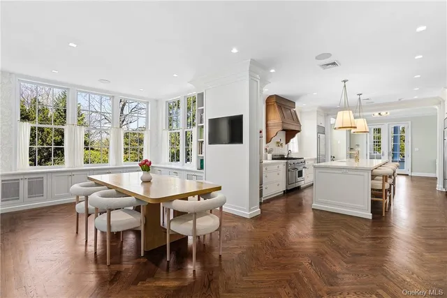 a dining room with kitchen island stainless steel appliances furniture a large window and a chandelier