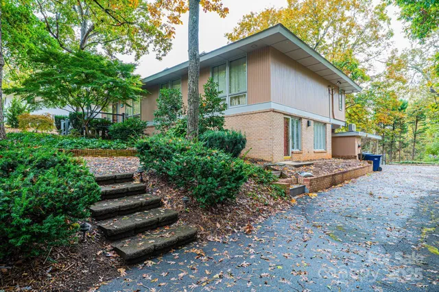 a view of a house with a yard plants and large tree