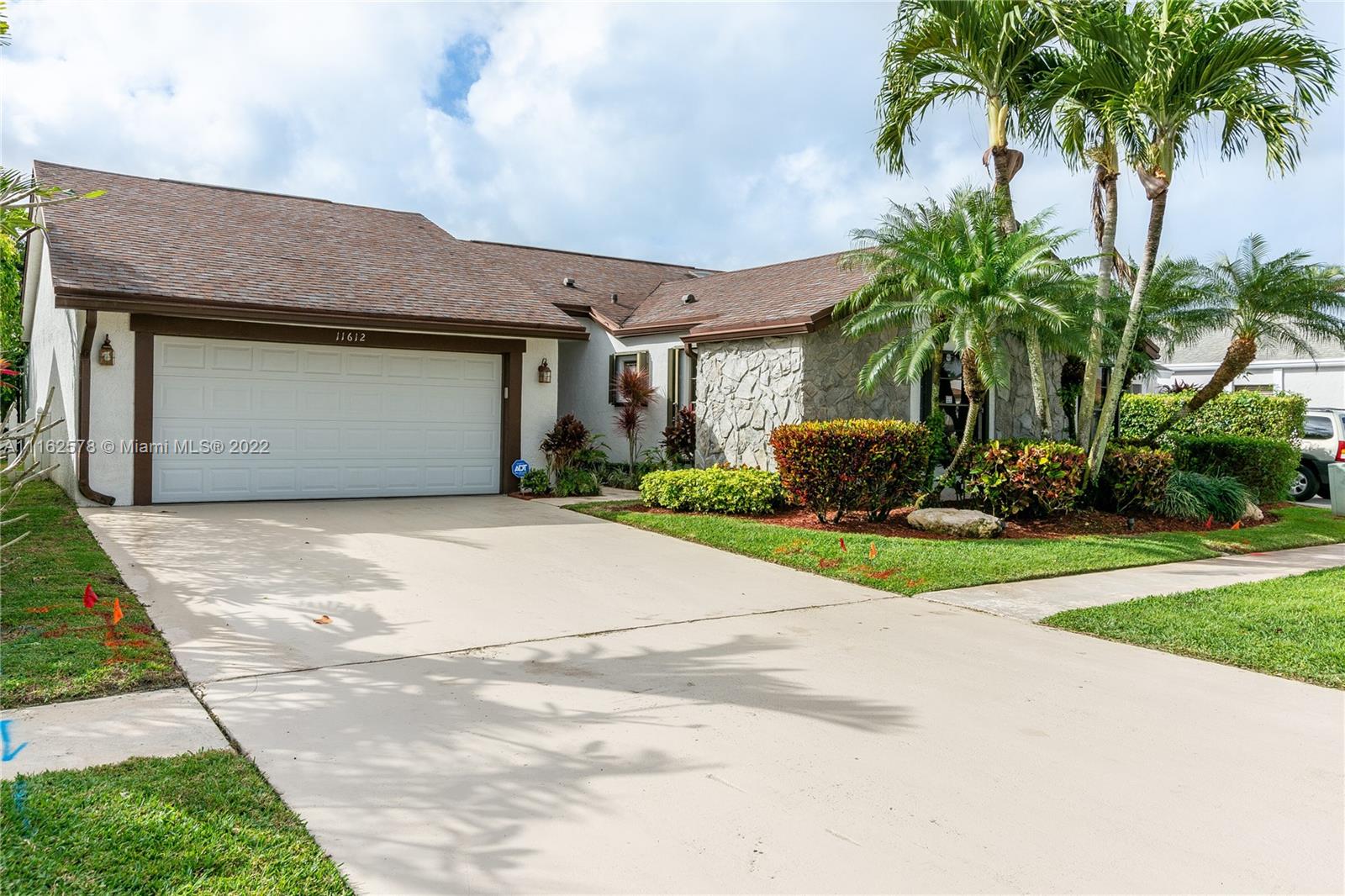 11612 Quiet Waters Lane Boca Raton, FL 33428 - Photo 2 of 70 a front view of a house with a garden and palm trees