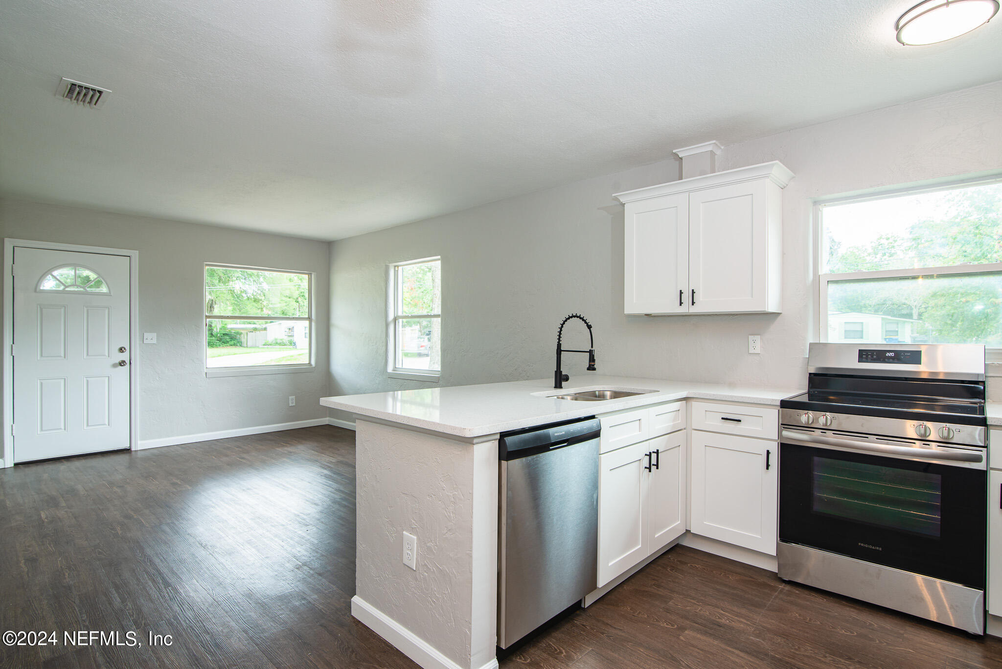 1702 King Arthur Road Jacksonville, FL 32211 - Photo 11 of 24 a kitchen with a stove a sink and white cabinets with wooden floor next to windows