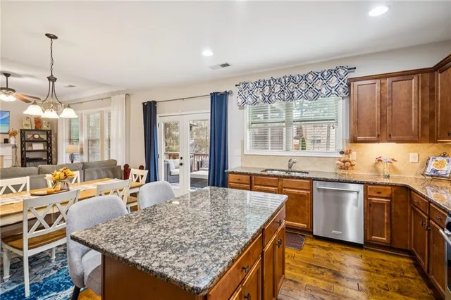 a kitchen with stainless steel appliances granite countertop a stove a sink dishwasher a refrigerator and a dining table with wooden cabinet