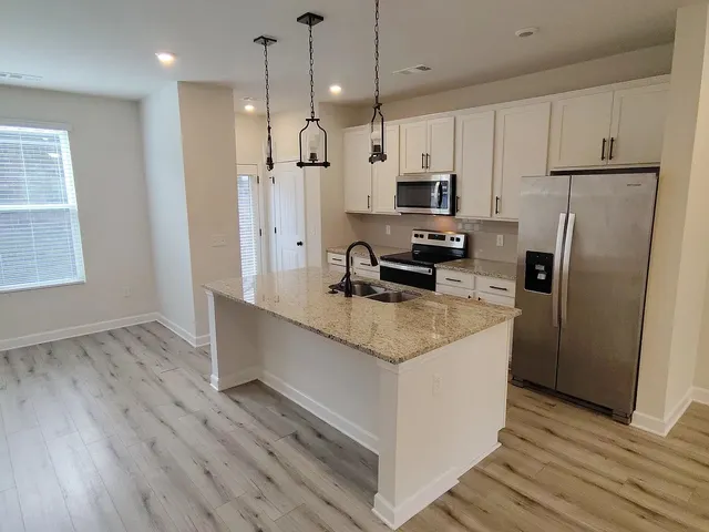 a kitchen with stainless steel appliances granite countertop a refrigerator a sink dishwasher a stove and white cabinets with wooden floor