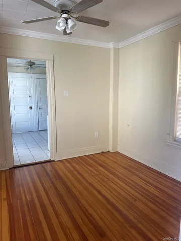 a view of an empty room with wooden floor and a ceiling fan