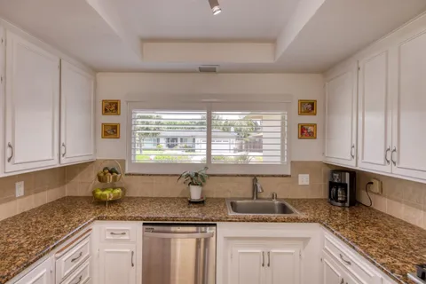 a kitchen with granite countertop a sink a window and cabinets
