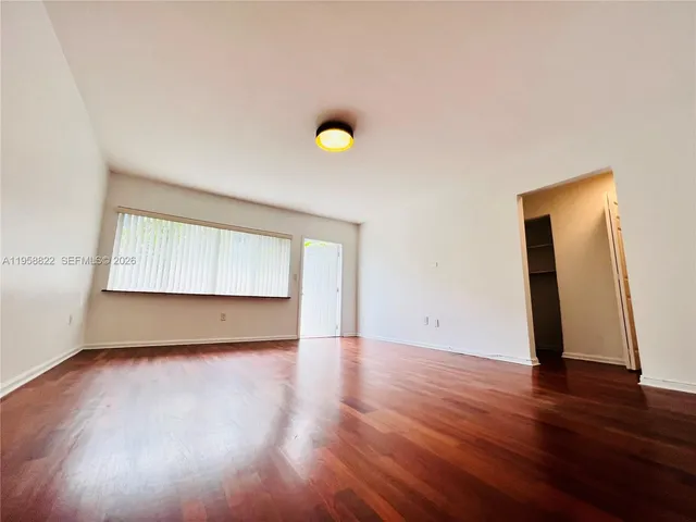 a view of an empty room with wooden floor and fan