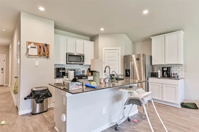a kitchen with stainless steel appliances kitchen island granite countertop a stove refrigerator a sink dishwasher and white cabinets with wooden floor
