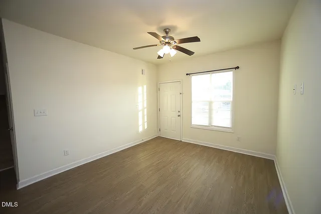 an empty room with wooden floor fan and windows