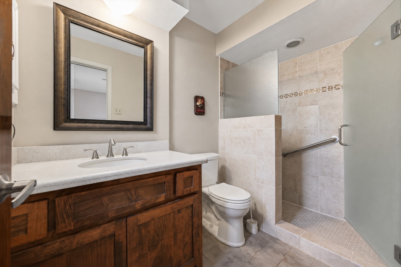1004 Wagon Road Simonton, TX 77485 - Photo 20 of 40 The recently remodeled primary bathroom vanity features a wide stone-look countertop with an undermount sink and brushed nickel faucet, offering a clean and elegant look. Rich wood cabinetry below provides ample storage, while a framed mirror and window above add brightness and a sense of space. This well-appointed vanity area sets a lovely tone for the full bathroom beyond.