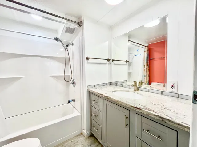 a bathroom with a granite countertop sink mirror bathtub and next to a window