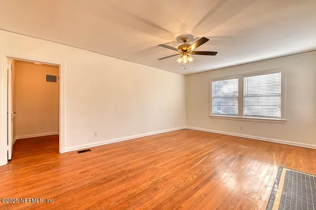 an empty room with wooden floor fan and windows