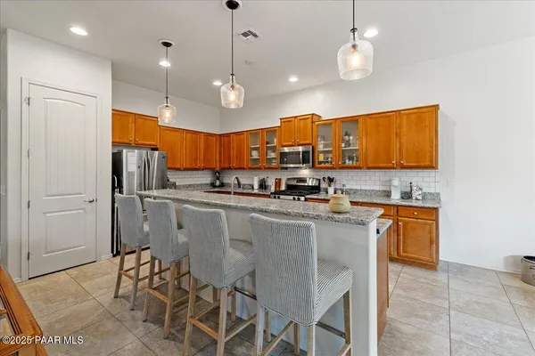 a kitchen with stainless steel appliances kitchen island granite countertop a sink a stove a refrigerator cabinets and chairs